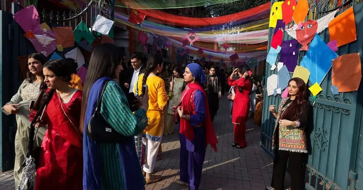 Festival-goers in bright kurtas and dupattas at a Lahore gateway hung with paper kites