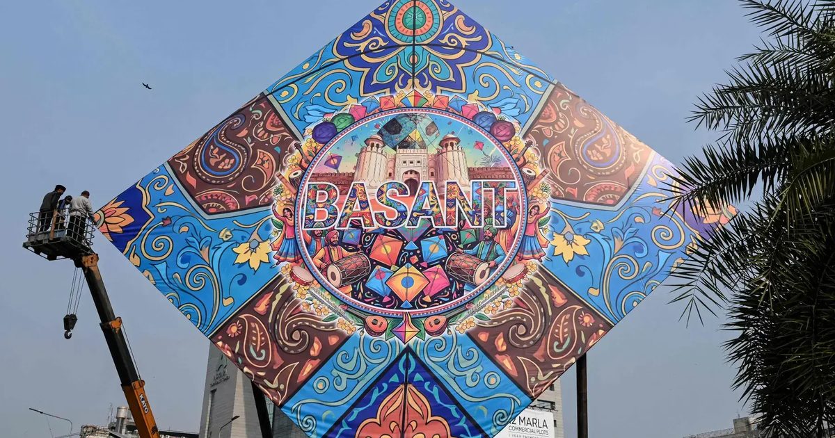 A large decorated Basant kite hoarding being raised by crane over a Lahore road