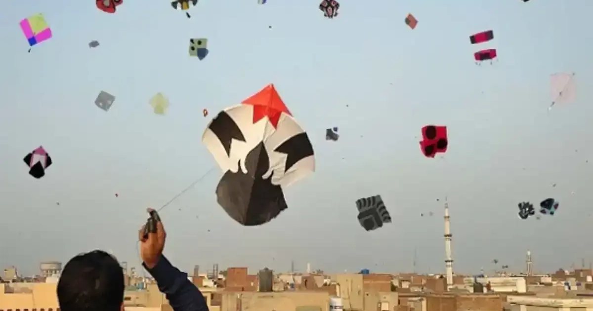 A man on a rooftop flying a kite, with dozens more kites in the sky above the city