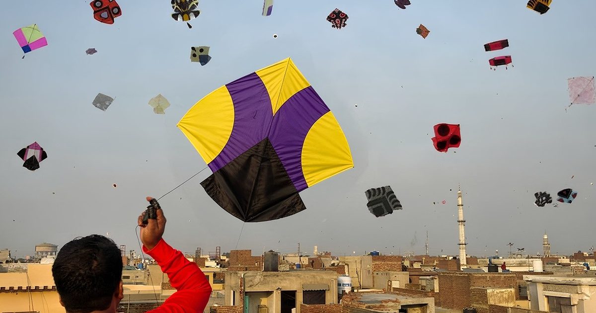 A flyer in red holding the line of a large purple and yellow gudda above Lahore rooftops