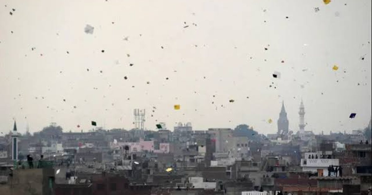 A dense mass of kites in a grey Lahore sky above the rooftops
