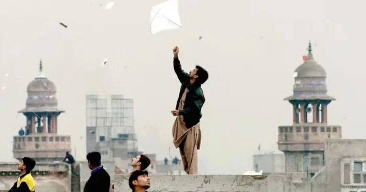 People standing on a Lahore rooftop flying kites above the old city